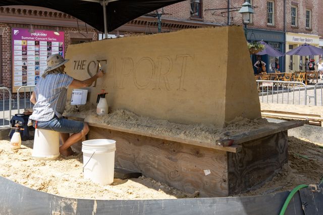 an artist carves into a sand sculpture outside the Seaport